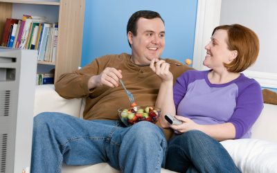 Overweight couple eating fruit on sofa