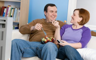 Overweight couple eating fruit on sofa