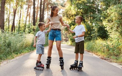 Outdoor shot of happy family having fun and roller skating together in summer park, mommy holding kids hands, being glad to spend weekend together, active pastime.