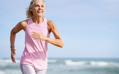 Older female doing sport to keep fit. Mature woman running along the shore of the beach. Concept of healthy living in the elderly. Senior woman in fitness clothing running along beach