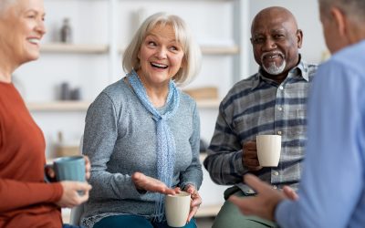 Multiracial group of positive senior men and women sitting in circle, drinking tea and having conversation, smiling and laughing, having home party or enjoying time at nursing home, closeup