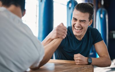Strong, active and men arm wrestling in the gym on a table while being playful for a challenge. Rivalry, game and male people or athletes doing strength muscle battle for fun, bonding and friendship