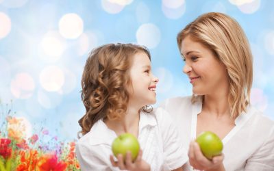 people, family, healthy eating and parenting concept - happy mother and daughter with green apples over poppy field background